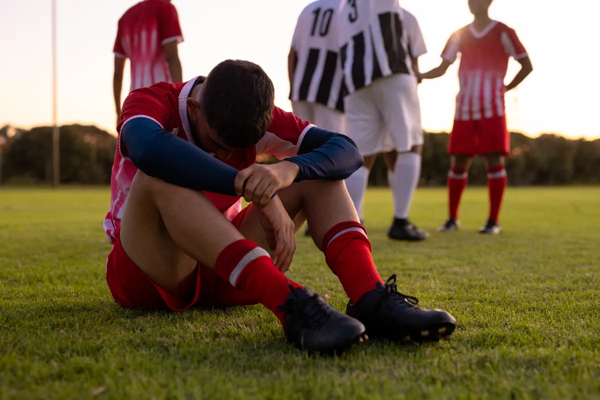 Futbolista profesional sentado en el césped tras perder un partido importante en el Mundial de fútbol.